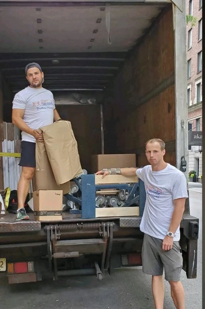 Two movers posing with equipment at the back of truck.