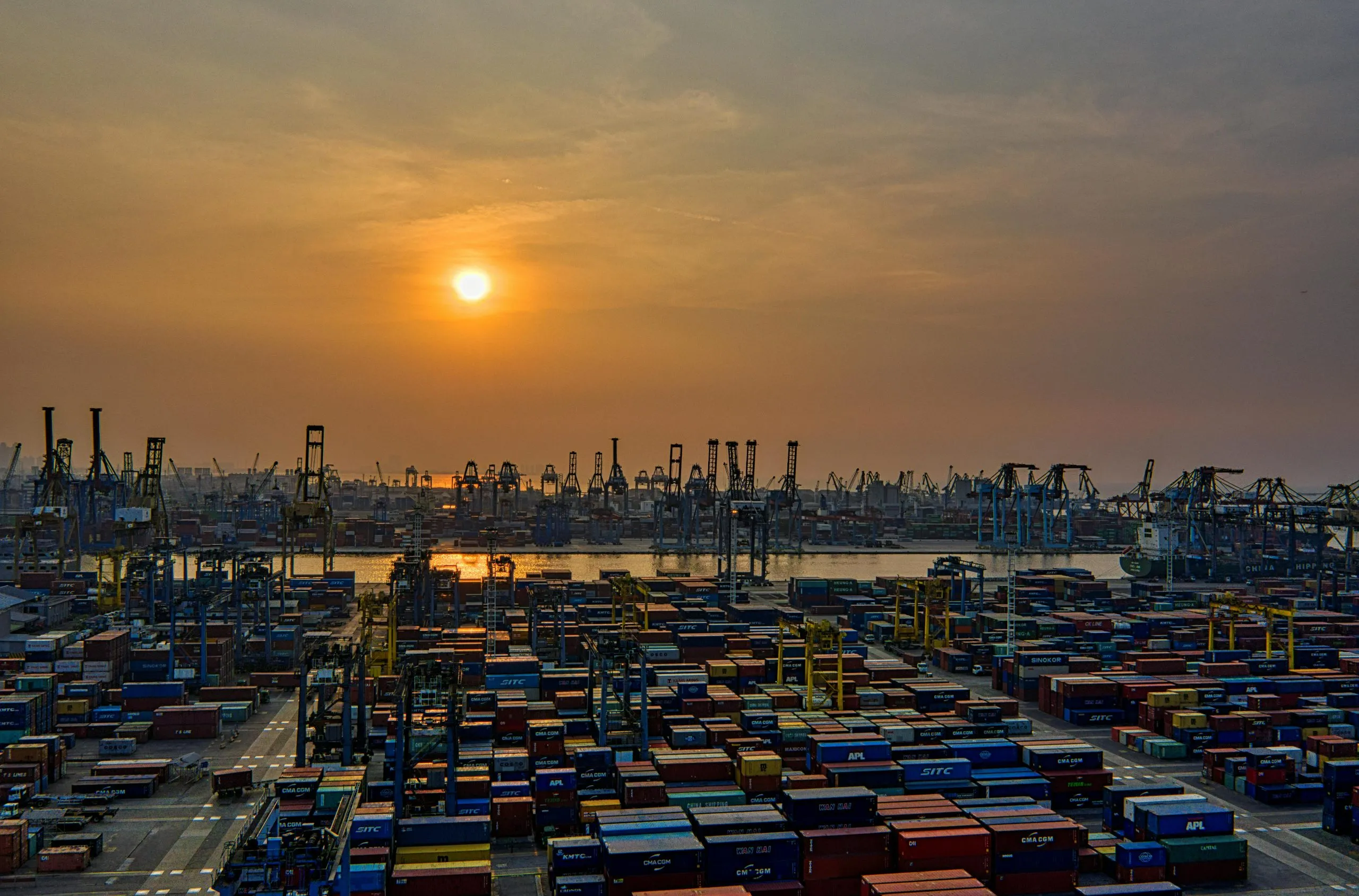Wide shot of busy shipping port with containers at sunset.