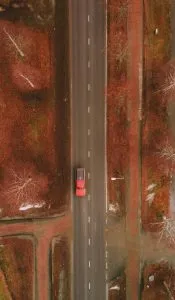 Top-down aerial view of red truck driving on autumn road.