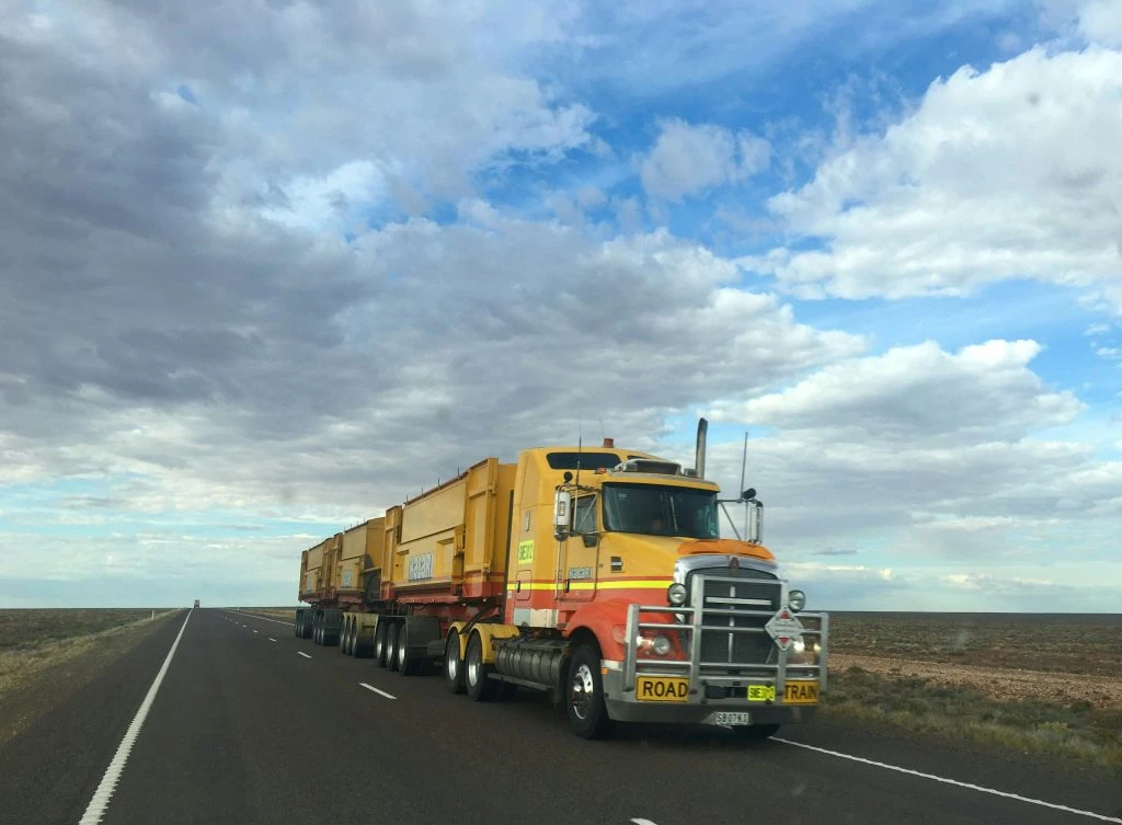 Large yellow road train truck driving on an open highway.